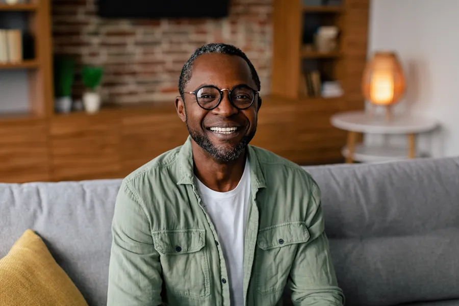 Andropause-Doctor A middle aged black man in a green button up shirt sits on his couch smiling, happy with his treatment for andropause and low testosterone from Scott Gulinson, MD, FACOG in Phoenix.