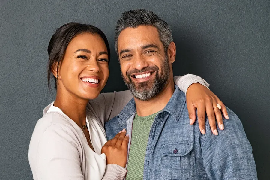 Bioidentical-Hormone-Therapy-Doctor A middle-aged couple with their arms around each other standing against a gray background and smiling, happy with the bioidentical hormone therapy they received from Scott Gulinson, MD, FACOG in Phoenix.