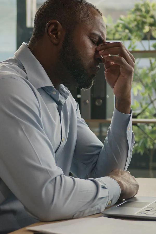 Chronic-Fatigue-Treatment A black man rubbing the top of his nose at his desk, in need of chronic fatigue treatment from Scott Gulinson, MD, FACOG in Phoenix.