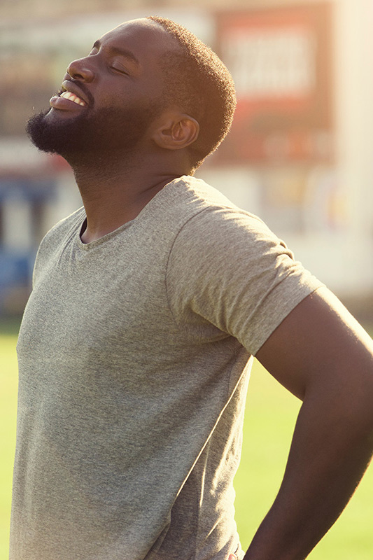 Lean-Muscle-and-Recovery-Treatment A black man in a gray t-shirt and smiles, looking up with closed eyes after a satisfying workout. Get treatment for lean muscle loss and recovery from Scott Gulinson, MD, FACOG in Phoenix.
