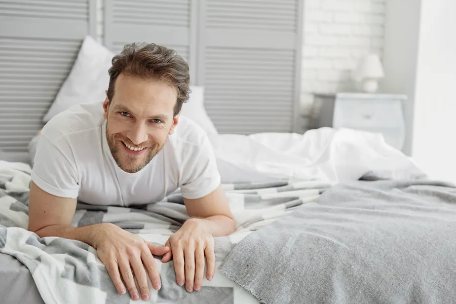 Low-Libido-in-Men-Doctor A dirty-blonde haired man lays on his stomach in bed smiling. Schedule treatment for low libido in men from Scott Gulinson, MD, FACOG in Phoenix.