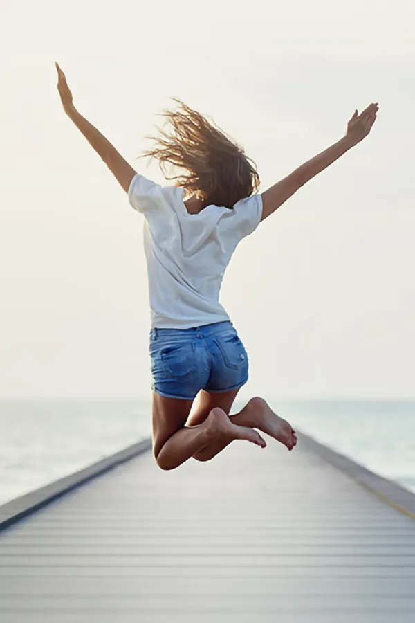 Perineoplasty-Treatment A woman jumping for joy on a pier. Get perineoplasty treatment from Scott Gulinson, MD, FACOG in Phoenix.
