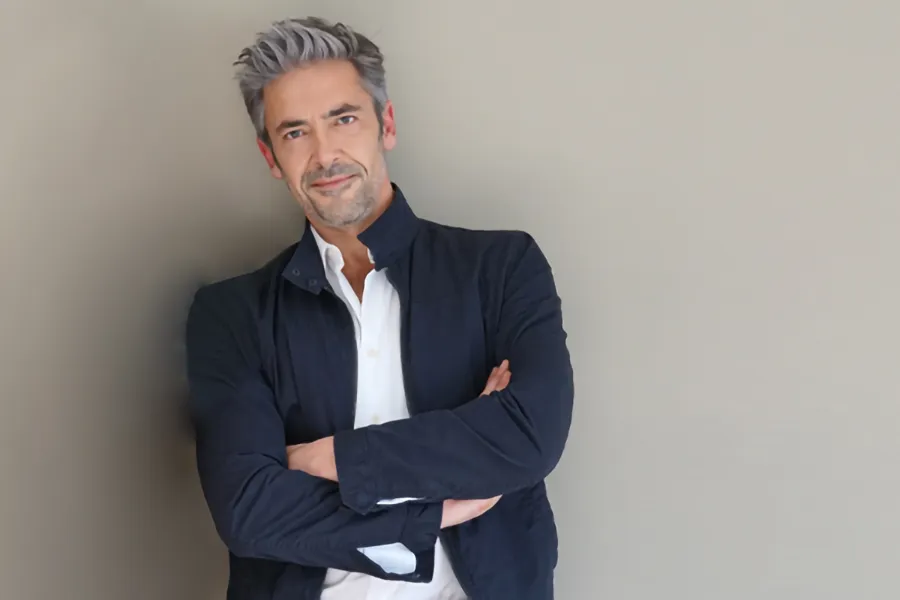 Testosterone-Low-T-Solutionsn-Clinic A middle-aged man in a white shirt and dark blue jacket leans against a gray wall smiling. Get testosterone for Low T from Scott Gulinson, MD, FACOG in Phoenix.