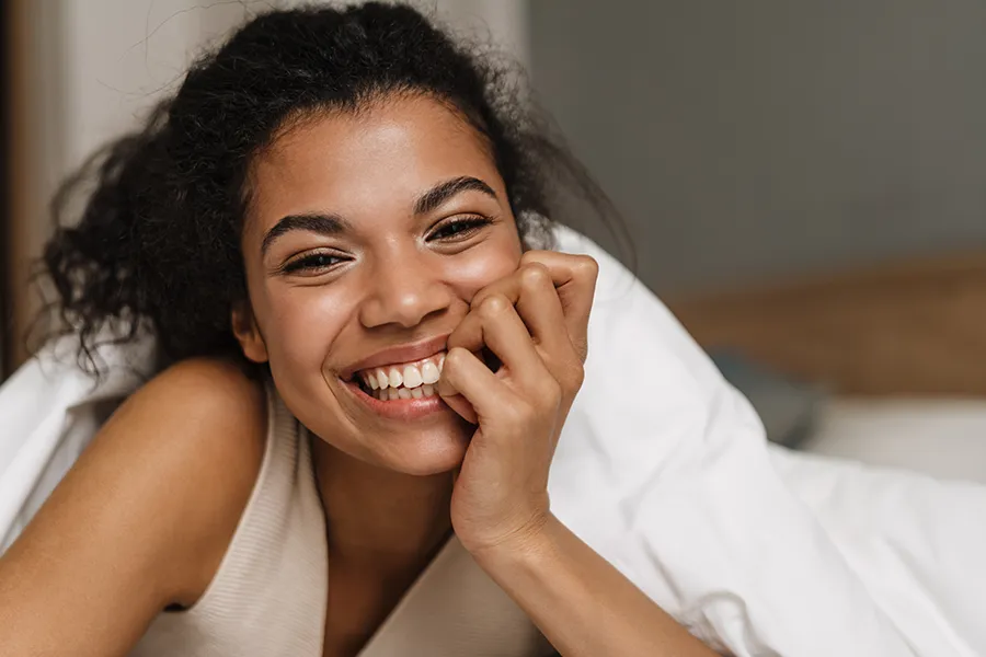 Vulvar-Labiaplasty-Clinic A woman laying under the covers and smiling. Smiling vulvar labiaplasty treatment from Scott Gulinson, MD, FACOG in Phoenix.