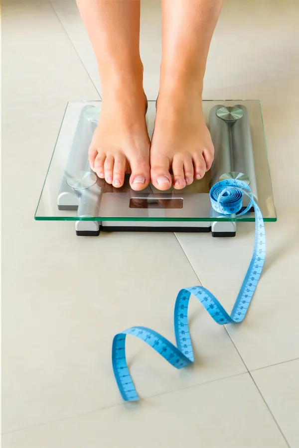Weight-Loss-Resistance-Treatment Close-up of a woman's feet standing on a scale, with measuring tape by her toes, getting treatment for weight loss resistance from Scott Gulinson, MD, FACOG in Phoenix.